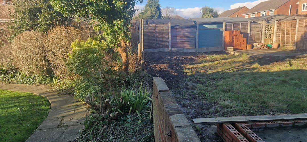 Overgrown rear garden boundary before fence installation at a 1970s Surrey fixer-upper renovation project.