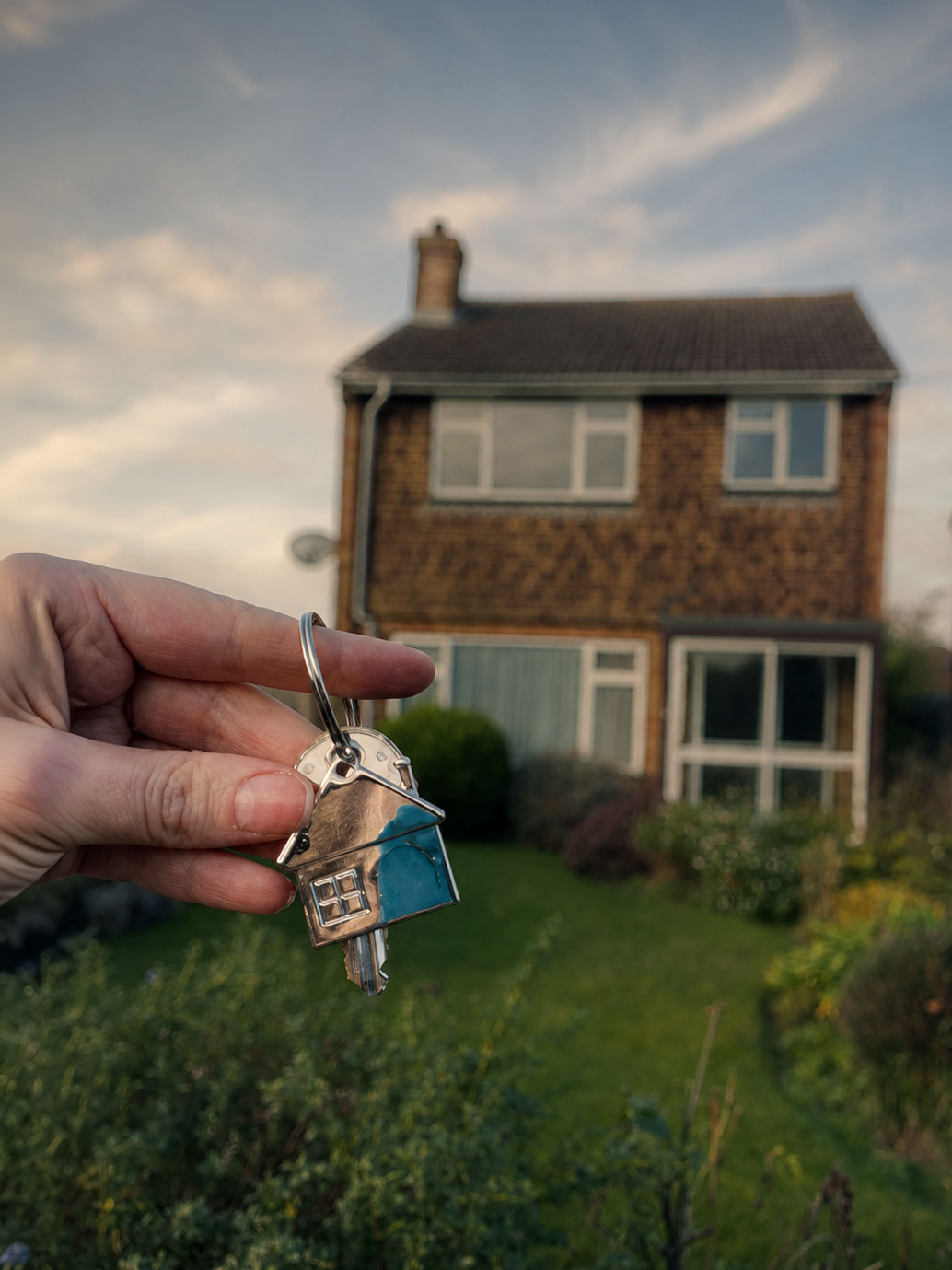 Holding keys to a 1970s detached house in Surrey with the garden in the background