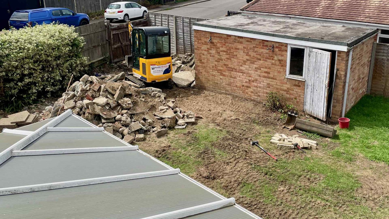 Mini digger removing an old concrete driveway during a Surrey family garden transformation project.