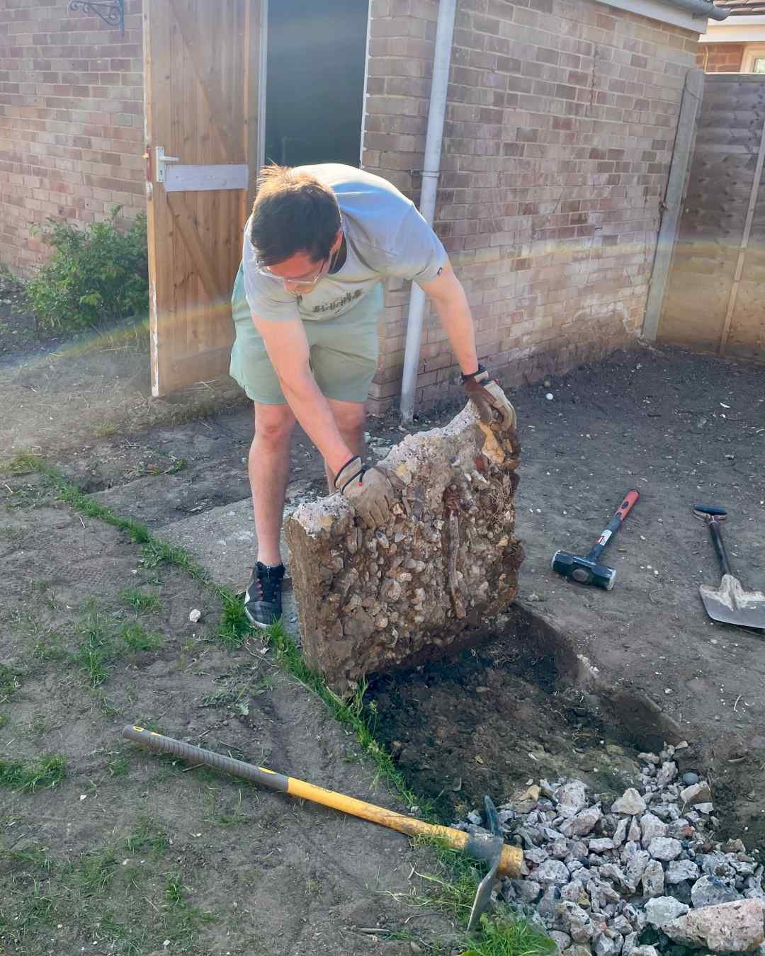 Removing the Old Pathway by Hand Removing a large section of old concrete pathway by hand during a Surrey family garden renovation.